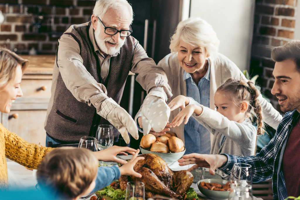 happy family reaching for turkey on thanksgiving table