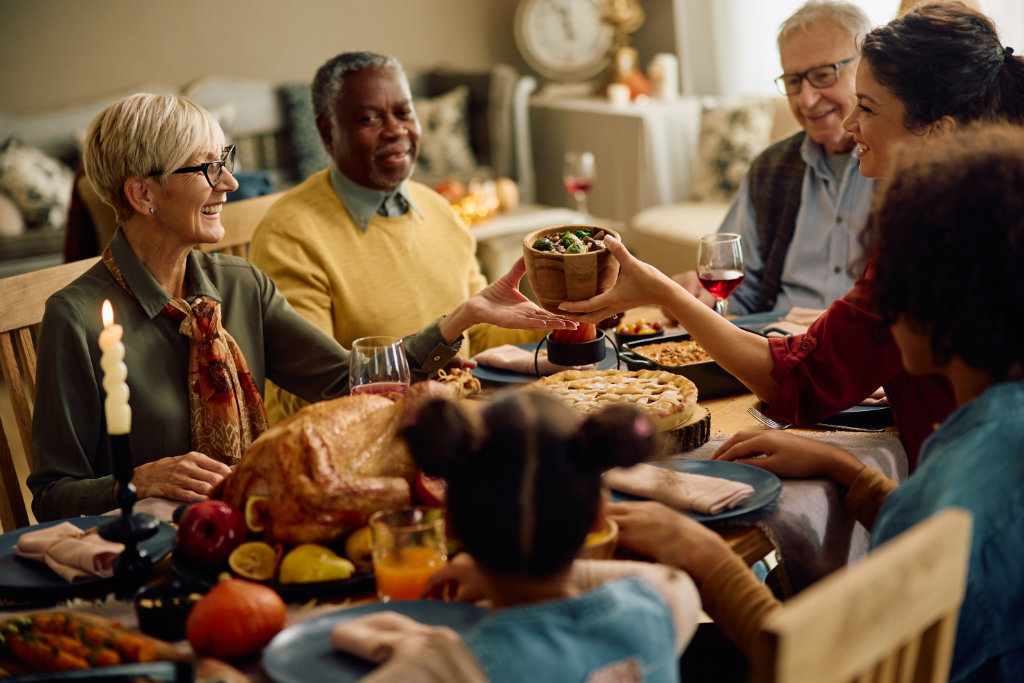 Happy woman serving food at dining table during Thanksgiving family dinner.