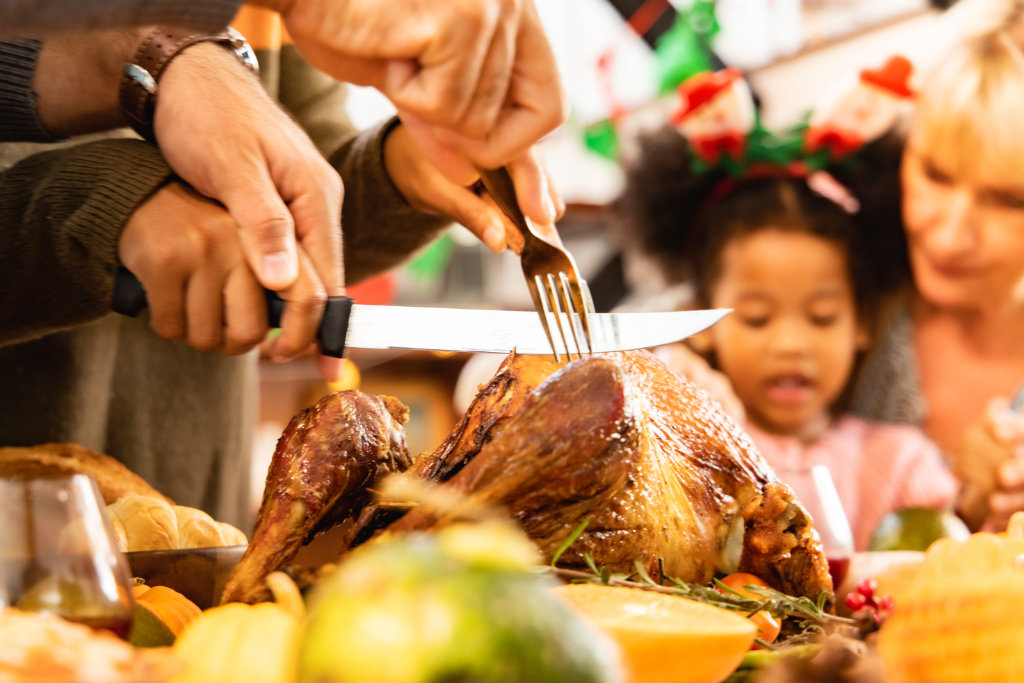 Thanksgiving Celebration Tradition Family Dinner Concept.family having holiday dinner and cutting turkey.Young black adult woman and her daughter happy.