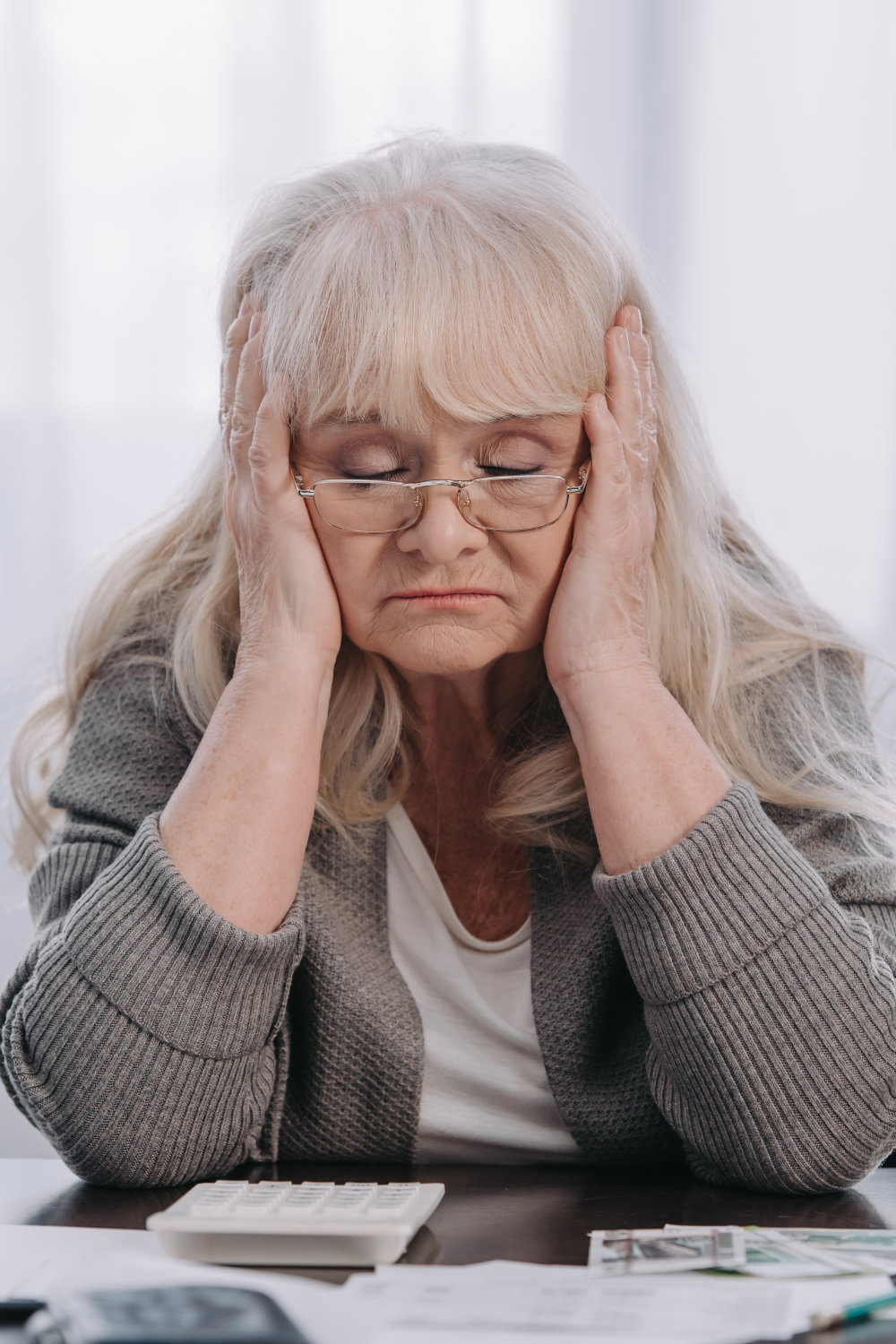 Stressed senior woman sitting at table with money and paperwork